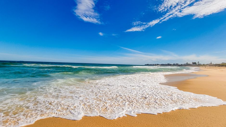 Relaxing beach scene with gentle waves and a vibrant blue sky on a sunny day.