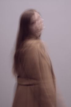 Artistic blurred portrait of a woman in motion wearing a brown coat, creating an ethereal and dreamlike effect.