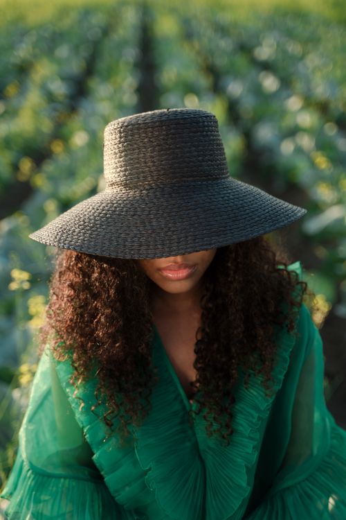 Free Stylish woman wearing a wide brim hat and green dress in an agricultural field. Stock Photo