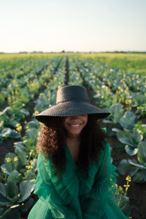 Free Smiling woman in green dress and hat sitting in a cabbage field, enjoying the outdoors. Stock Photo