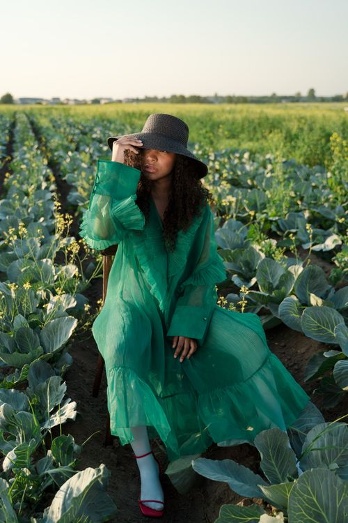 Free A woman in a wide-brim hat sits in a verdant cabbage field, blending fashion with nature. Stock Photo