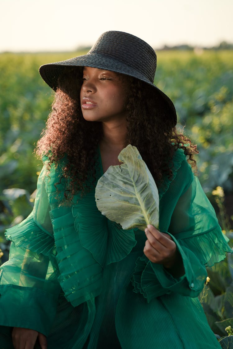 Portrait Of Woman In Green Dress And Wide Brim Hat Sitting In Cabbage Field