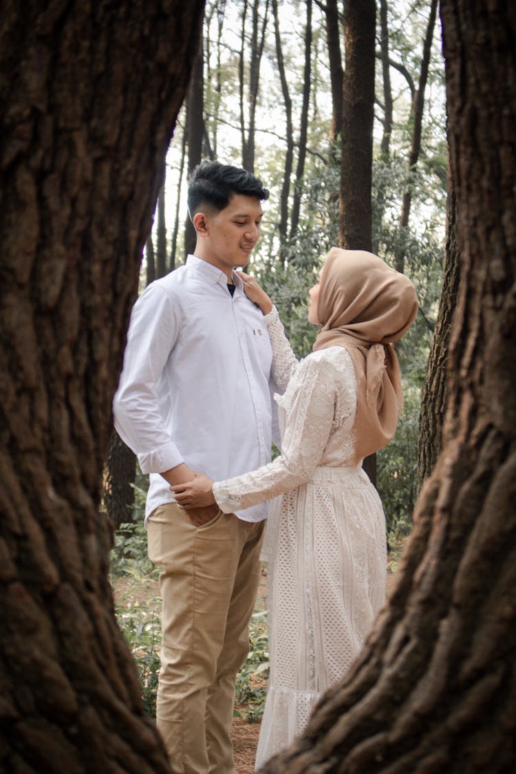 A Couple Standing Between Tree Trunks While Looking At Each Other