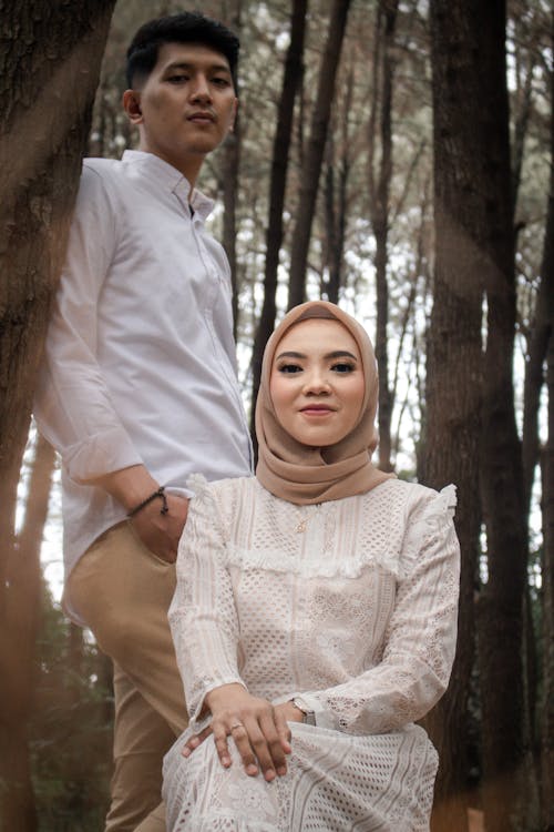 Free A Man Standing Behind a Woman with Hijab Sitting Near a Tree Stock Photo