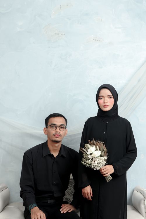 Free A couple in black attire, one holding a bouquet, poses in a minimal indoor setting. Stock Photo