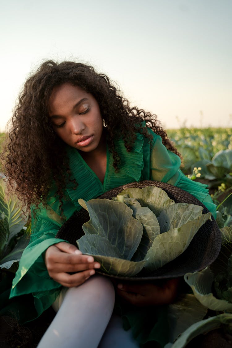 Woman With Long Curly Hair Holding Brown Straw Hat Full Of Cabbage Leaves