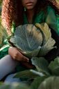 Unrecognizable Woman Embracing Straw Hat Full of Cabbage Leaves
