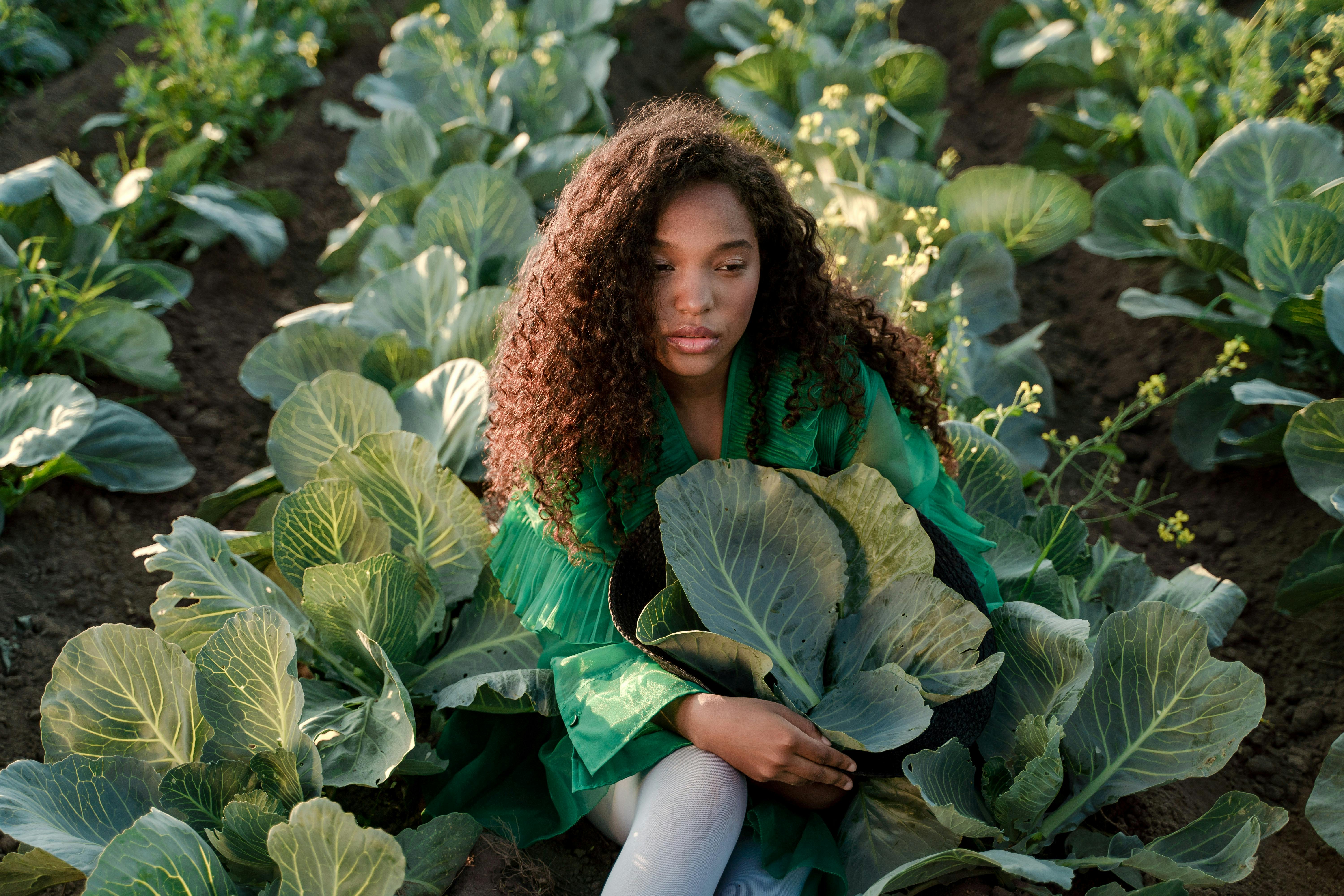 woman sitting on ground and embracing brown hat full of cabbage leaves