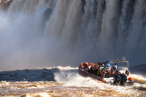 People Riding on Orange Boat Near the Waterfall