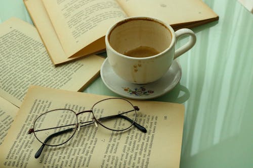 Free A Ceramic Cup and Saucer Near the Open Books with Eyeglasses Stock Photo
