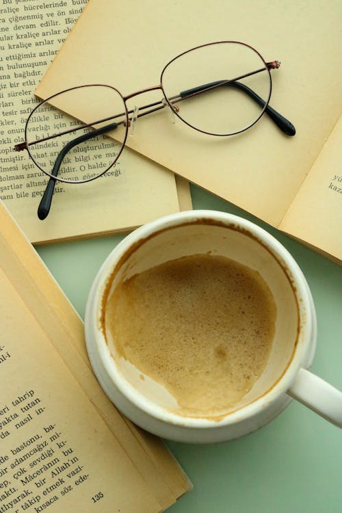 A Ceramic Cup with Coffee Near the Eyeglasses on the Book