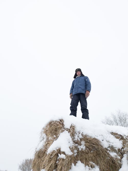 A Low Angle Shot of a Man in Blue Jacket Standing on a Snow Covered Ground