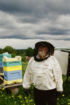 An experienced beekeeper standing by hives in protective gear