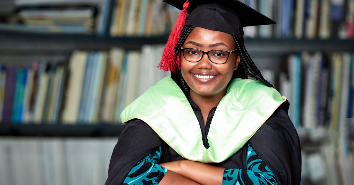 Smiling Woman in Glasses in Graduation Gown Sitting with Bookcase in ...