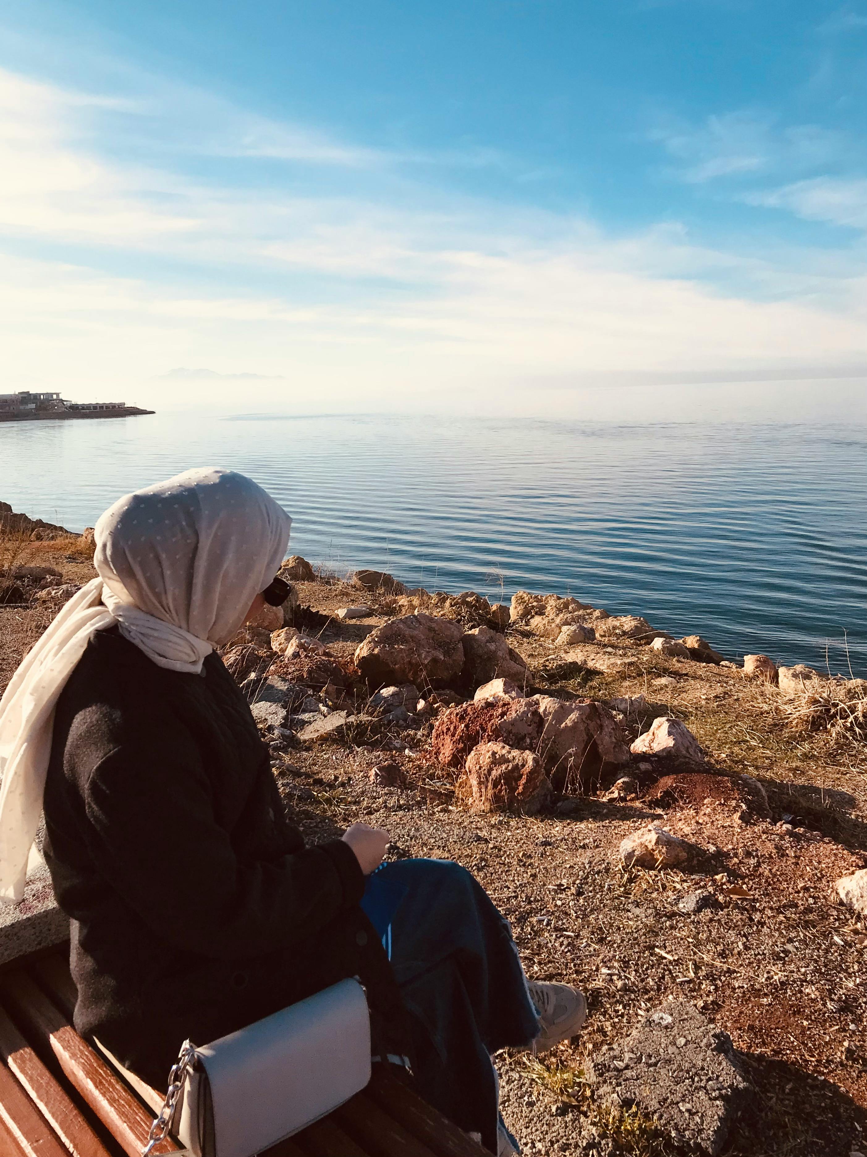 Person Wearing Headscarf Sitting on a Bench Near Body of Water · Free Stock  Photo