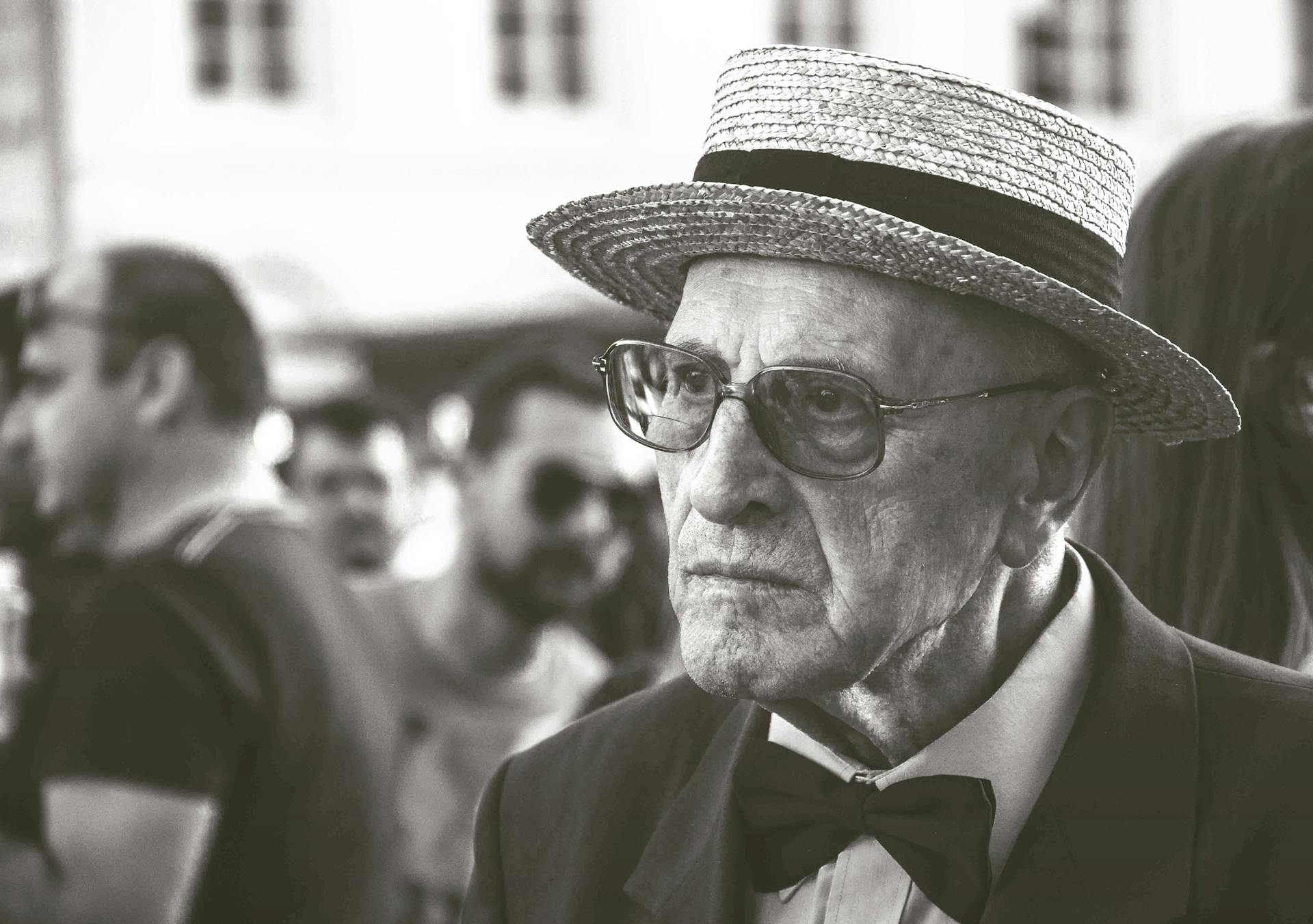 Black and white portrait of an elderly man wearing a straw hat and bow tie, exuding a serious expression.