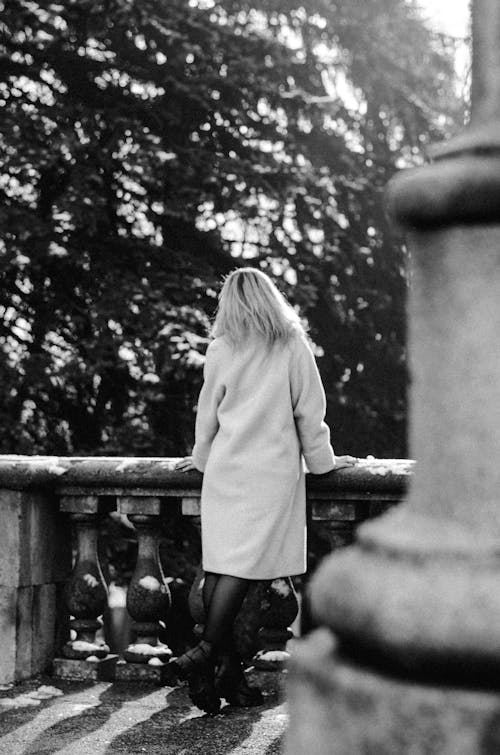Free Grayscale Photo of Woman in White Coat Standing Beside a Concrete Fence with Precast Stock Photo