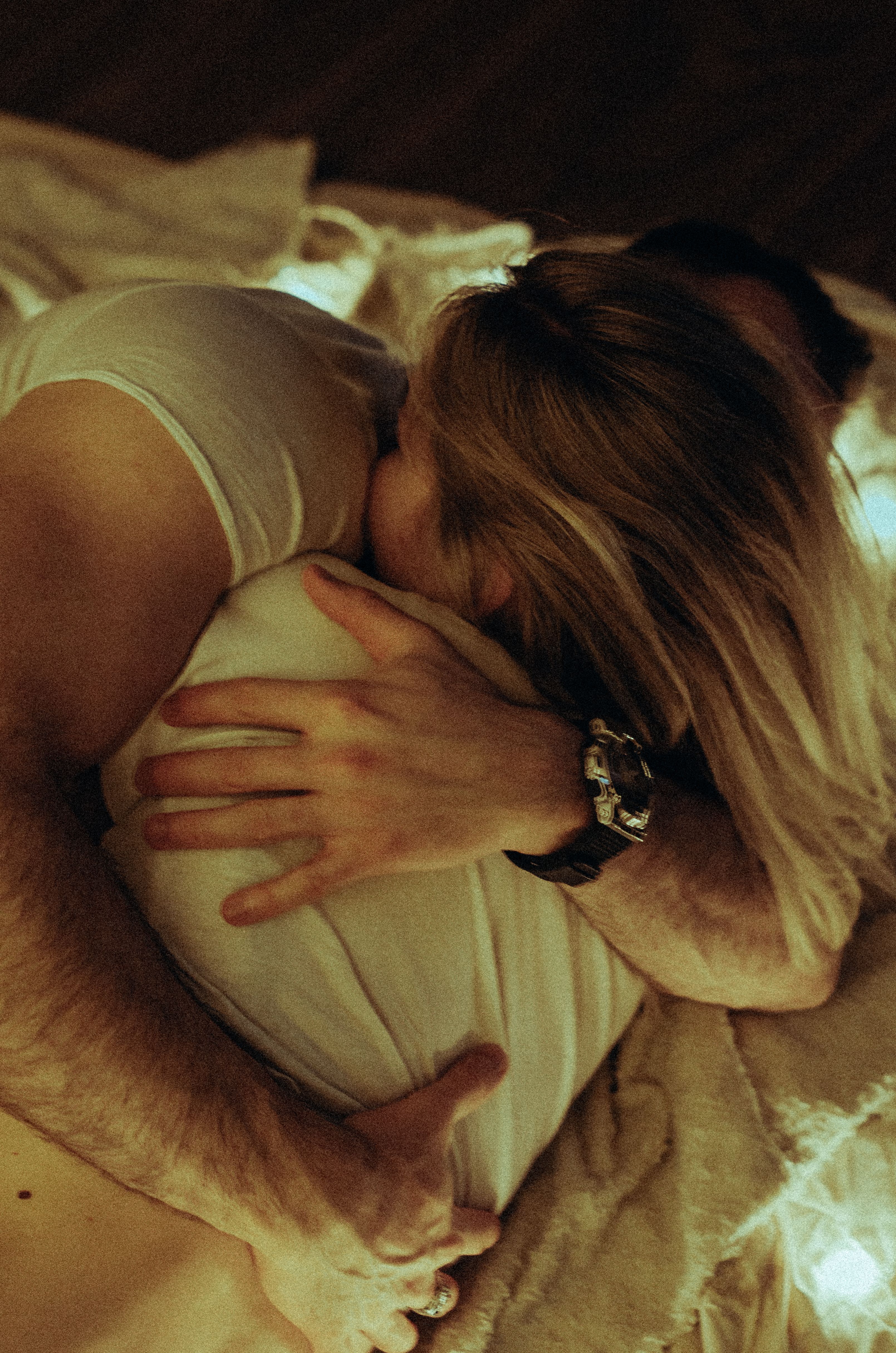 A tender moment captured as a couple embraces warmly on a cozy bed indoors.