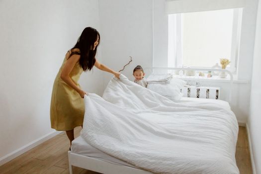 A mother and daughter making the bed in a bright, airy bedroom with white walls.