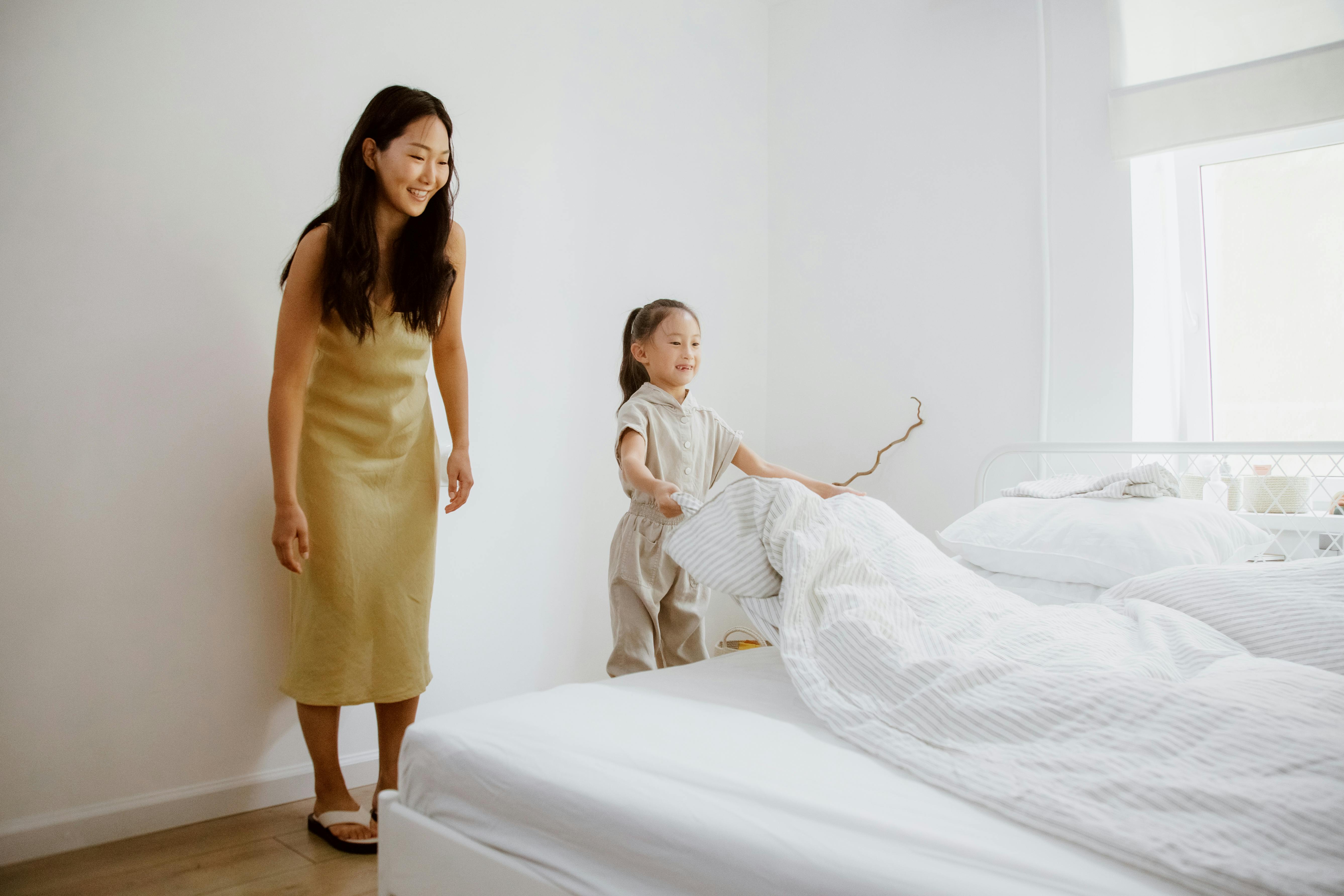 daughter making a bed and mother looking at her