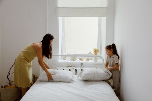 Free A mother and daughter making the bed together in a bright and cozy bedroom. Stock Photo