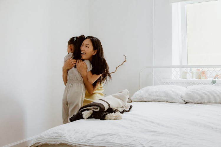 Mother And Daughter Hugging Next To Bed