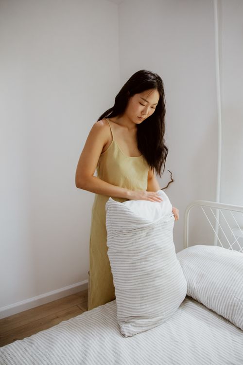 Free A woman setting up a bed in a bright, minimalist bedroom interior. Stock Photo