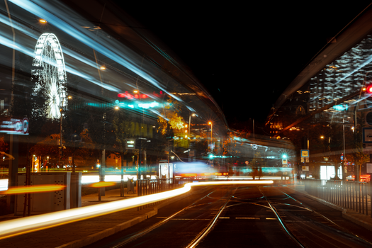 Long exposure of a city street at night featuring vibrant light streaks and an illuminated ferris wheel.