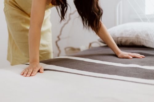 Free A woman making a bed adorned with striped linens in a bright, minimalist bedroom. Stock Photo