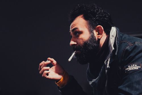 Free Side view of a bearded man smoking a cigarette at night, wearing a denim jacket. Stock Photo