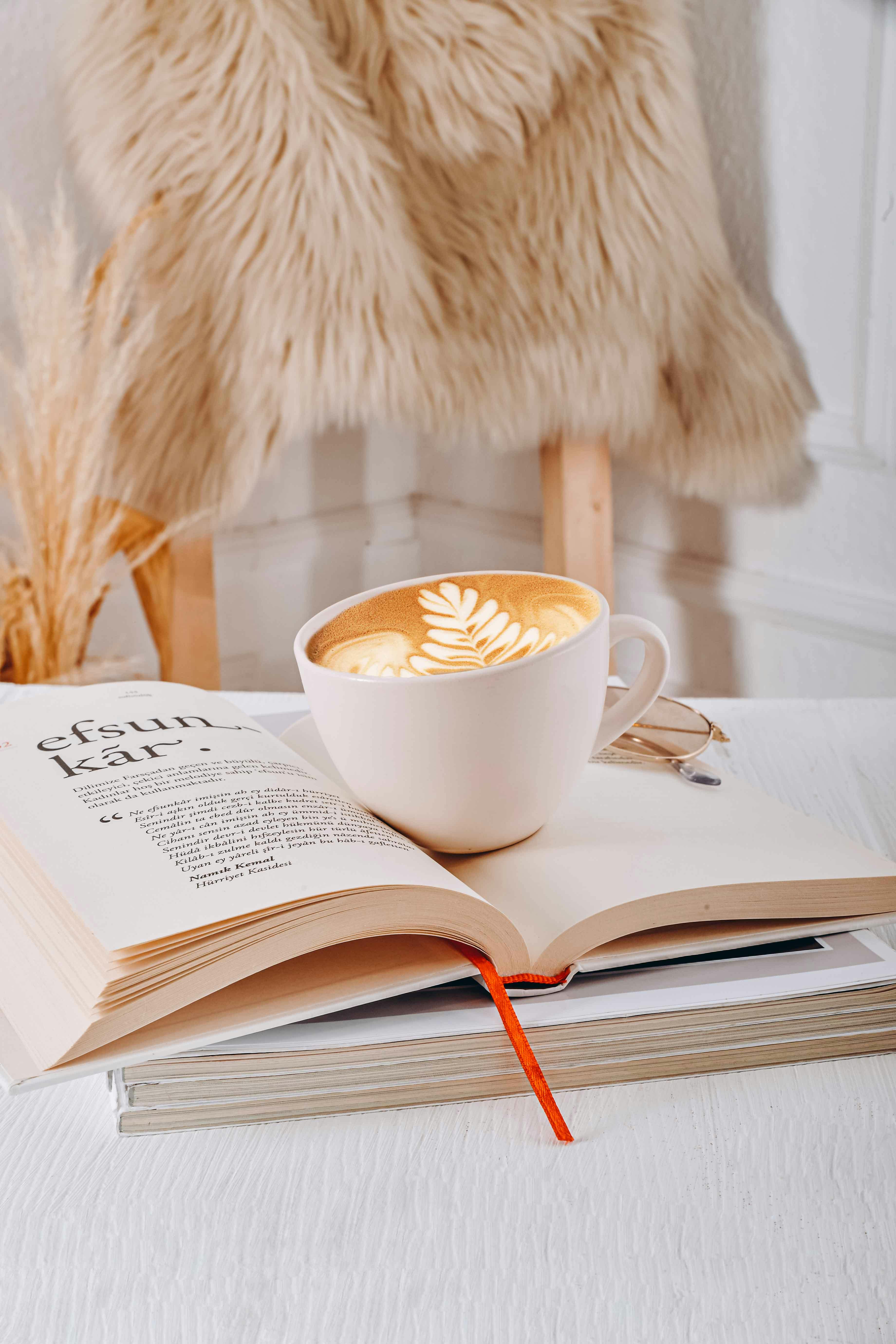 A warm, inviting scene featuring a coffee cup with latte art and an open book indoors.