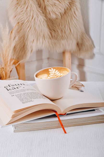 A warm, inviting scene featuring a coffee cup with latte art and an open book indoors.