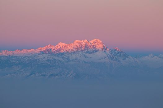 A stunning view of snow-capped mountain peaks glowing pink during sunset in a foggy landscape.