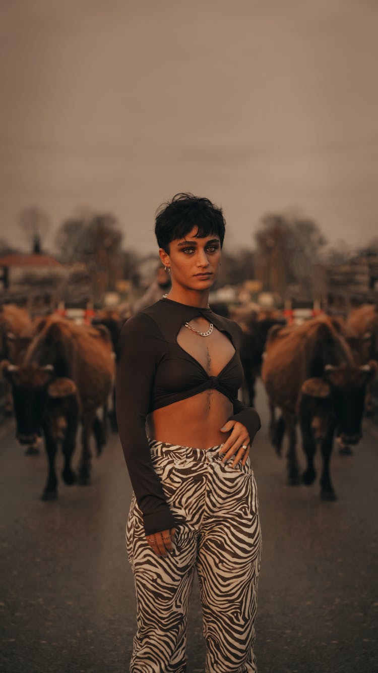 Fashionable Woman Standing On A Street On The Background Of A Walking Cattle Herd 