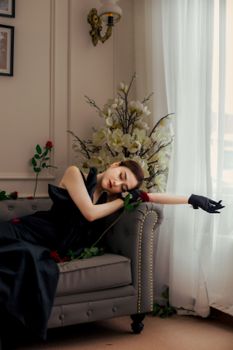 A woman in a black dress lies elegantly on a sofa, surrounded by red roses.