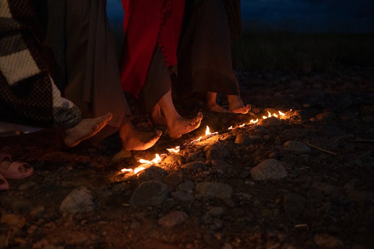 People  Heating Their Feet On A Burning Stick On Ground