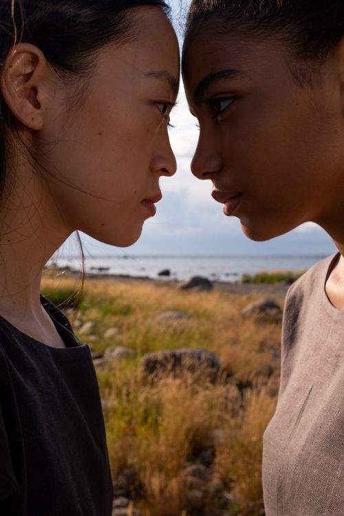Free Asian and African American women standing face to face outdoors, conveying intensity and diversity. Stock Photo