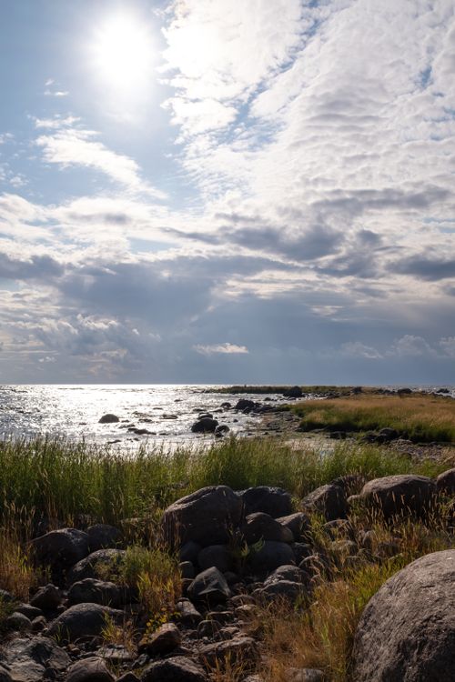 Free Beautiful rocky coastal view with cloudy sky and sunlight reflections on water. Stock Photo