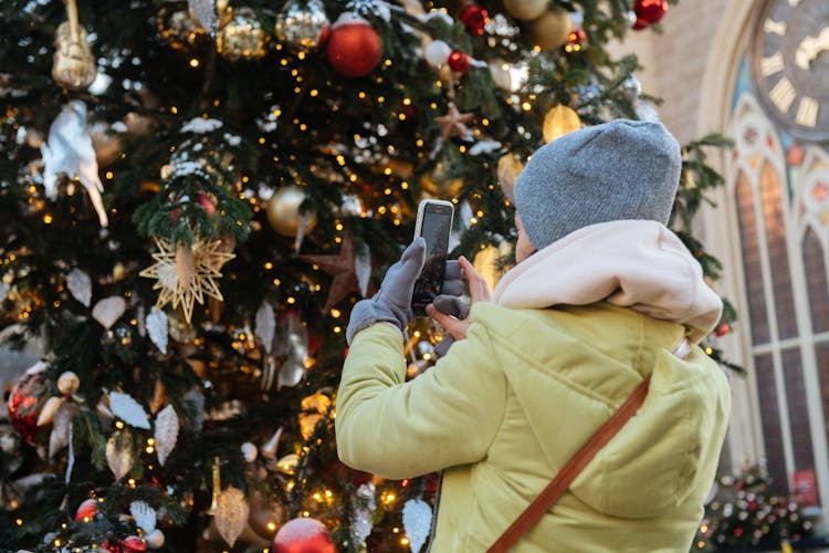 Unrecognizable Female Person In Winter Clothes Making Photo Of Decorated Christmas Tree