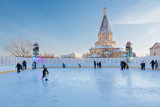 People enjoying ice skating at an outdoor rink in Moscow, with a church in the background.