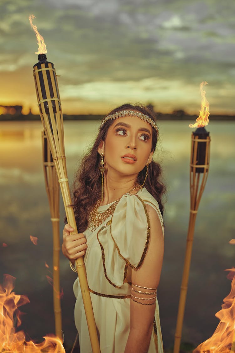 A Woman In Greek Dress Holding A Bamboo Holder With Oil Lamp 