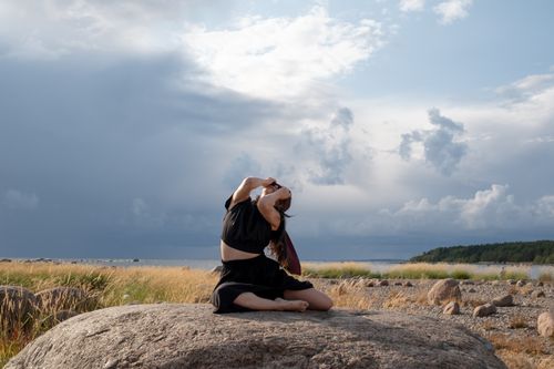 Free A woman performs a contemporary dance on a rock, surrounded by nature with a cloudy sky backdrop. Stock Photo