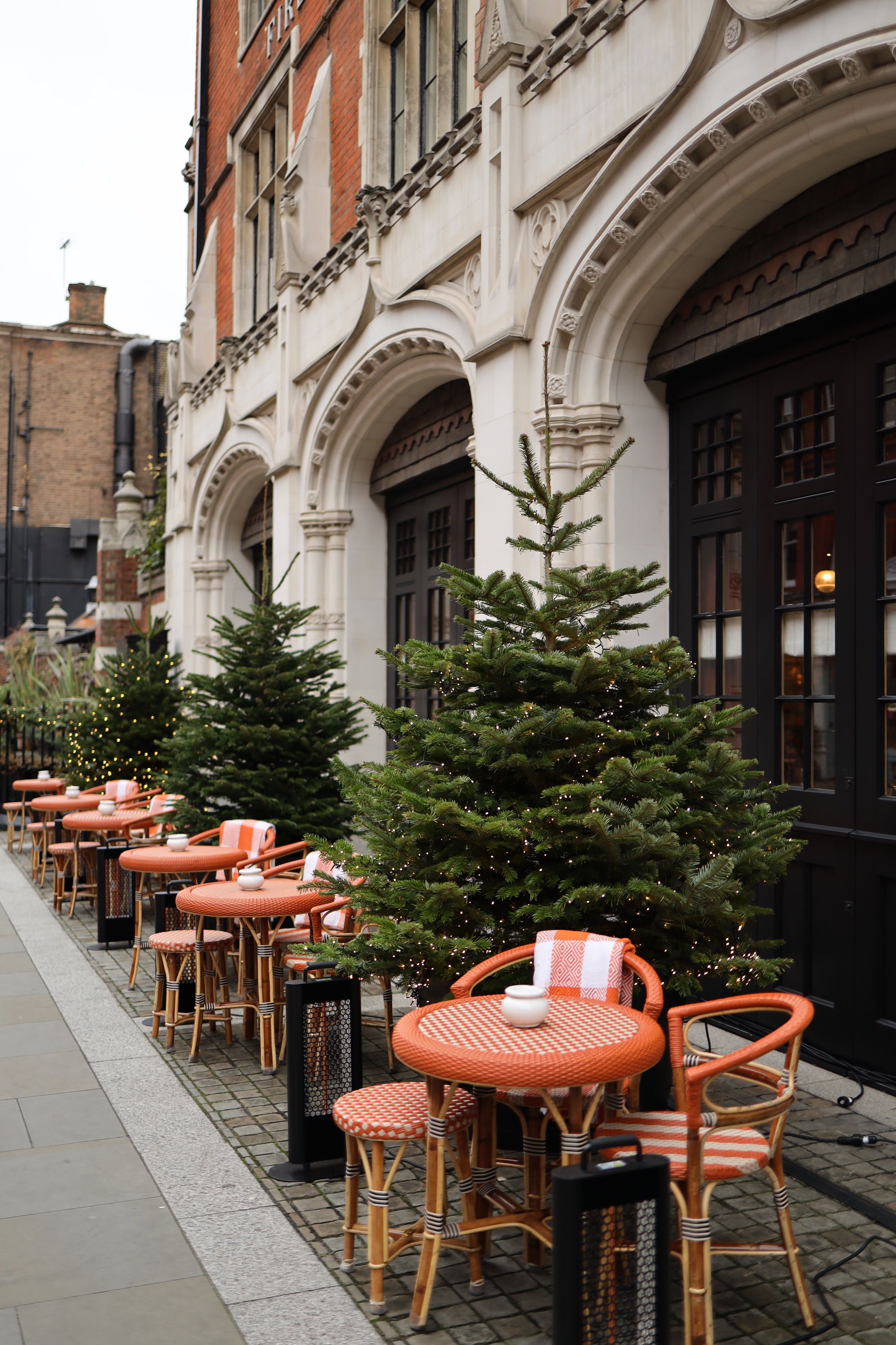 Quaint outdoor cafe adorned with festive Christmas trees and decorations.
