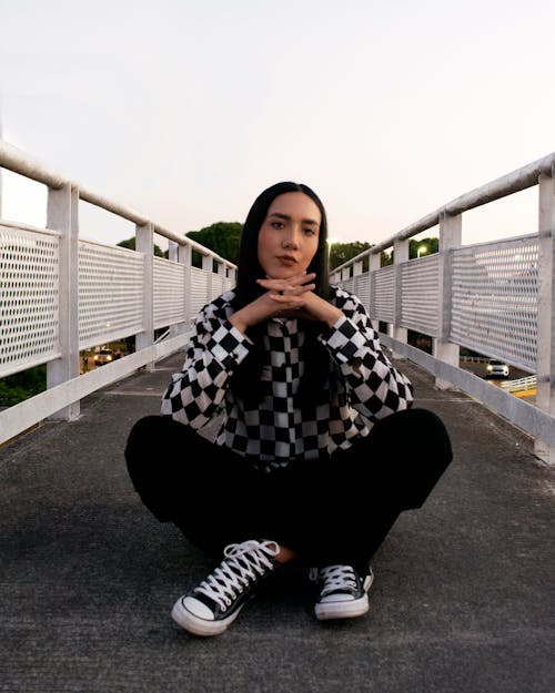 Woman in Black and White Checkered Long Sleeve Shirt and Black Pants Sitting on the Ground