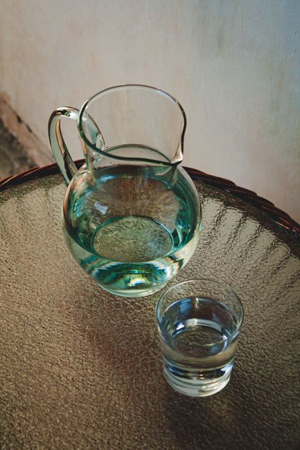 Fotomural Una jarra de agua clara y un vaso sobre una mesa de vidrio texturizada bajo luz natural.