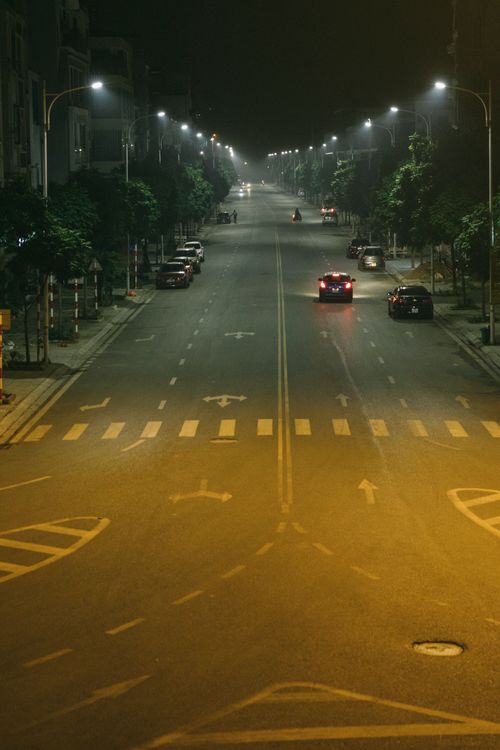 Free A quiet urban street at night with cars and streetlights casting a moody glow. Stock Photo