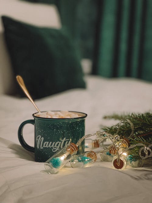 Green Ceramic Mug With Golden Spoon Beside Glass Bottles with String Lights 