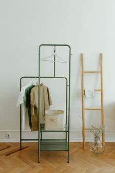 Simple and stylish home interior featuring a clothing rack, wooden ladder, and vase on a wooden floor.