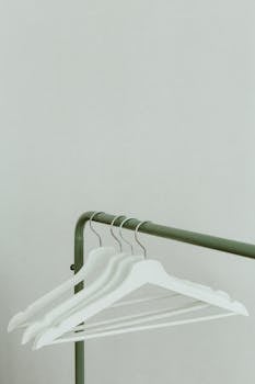 White hangers on a green metal clothing rack against a neutral wall.