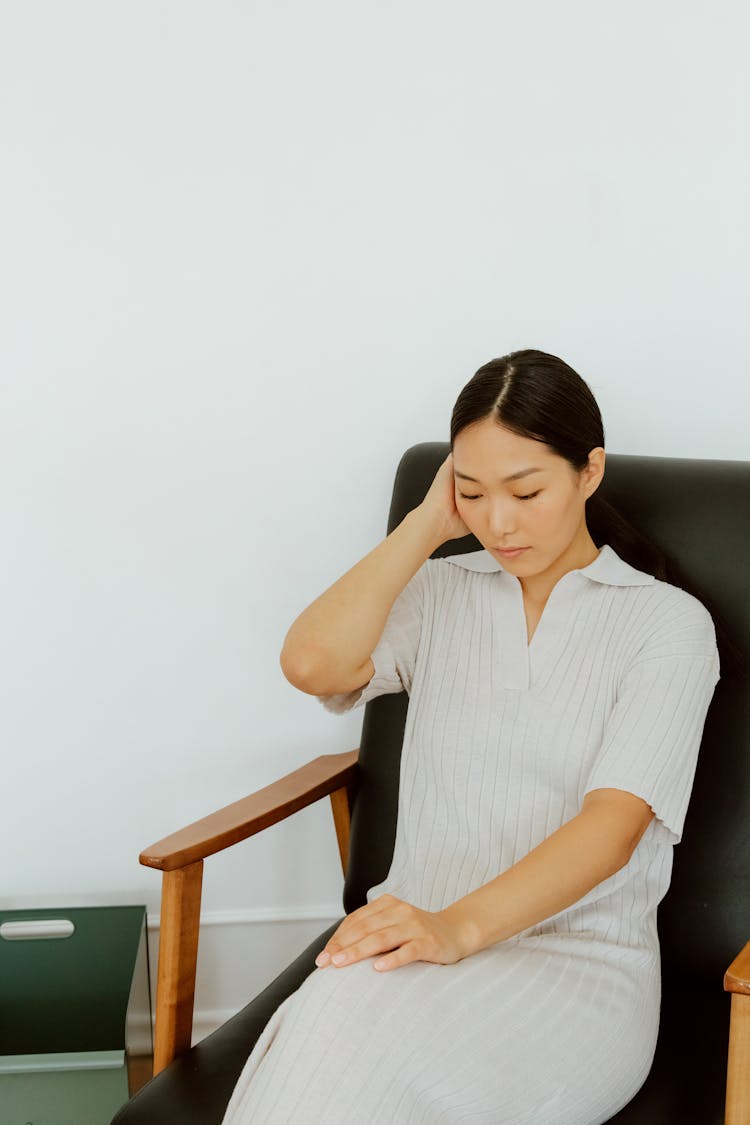 Woman Sitting In Armchair Touching Her Head